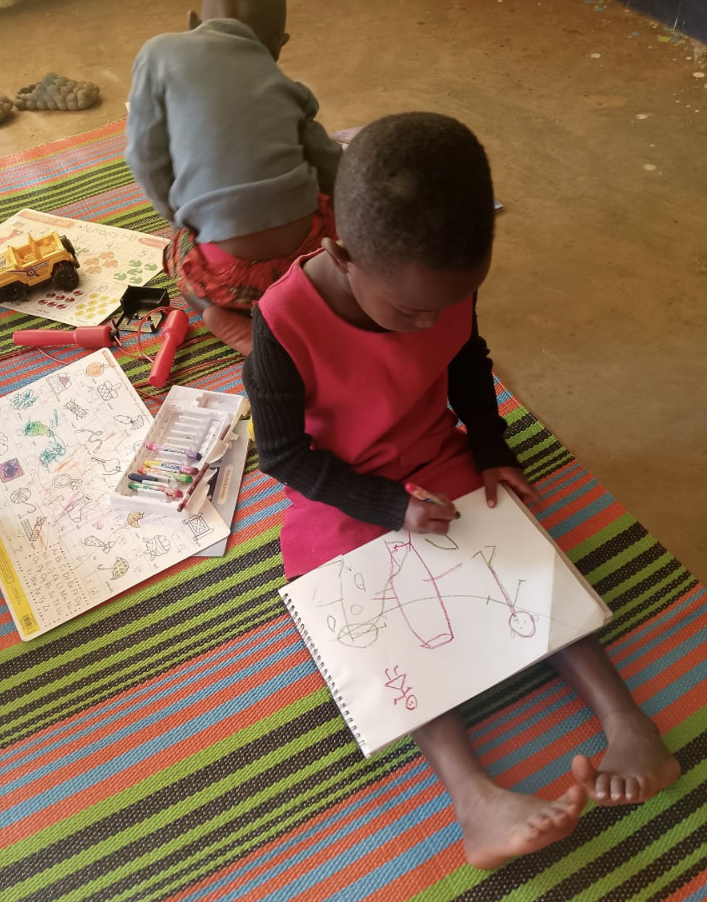 A young child drawing in a sketchbook on a striped mat