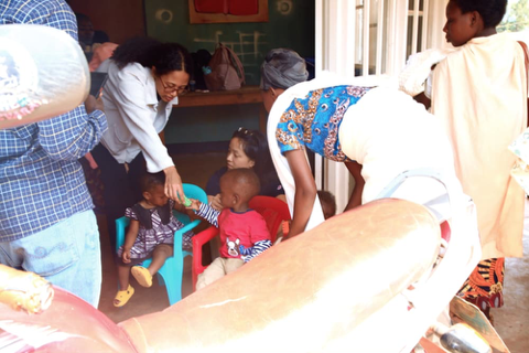 A volunteer helping a toddler drink while other children sit nearby