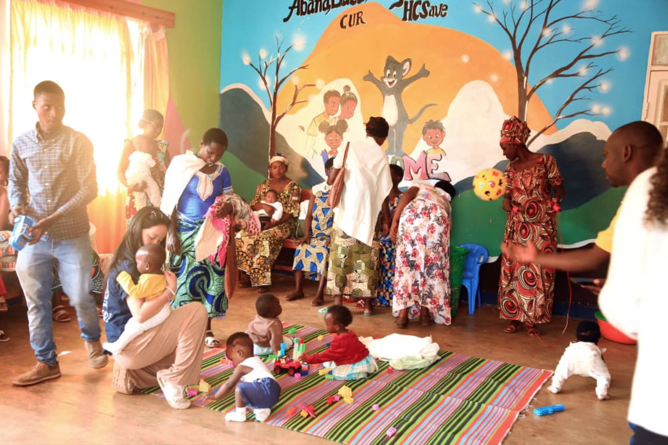 Mothers and caregivers in the colorful childcare room while babies play on a striped mat