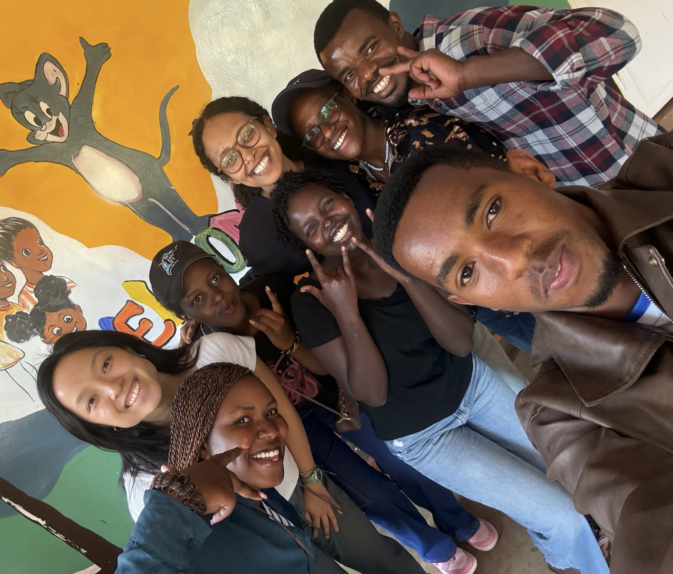 The 2026 Youth Impact Hub cohort smiling together in front of a painted mural