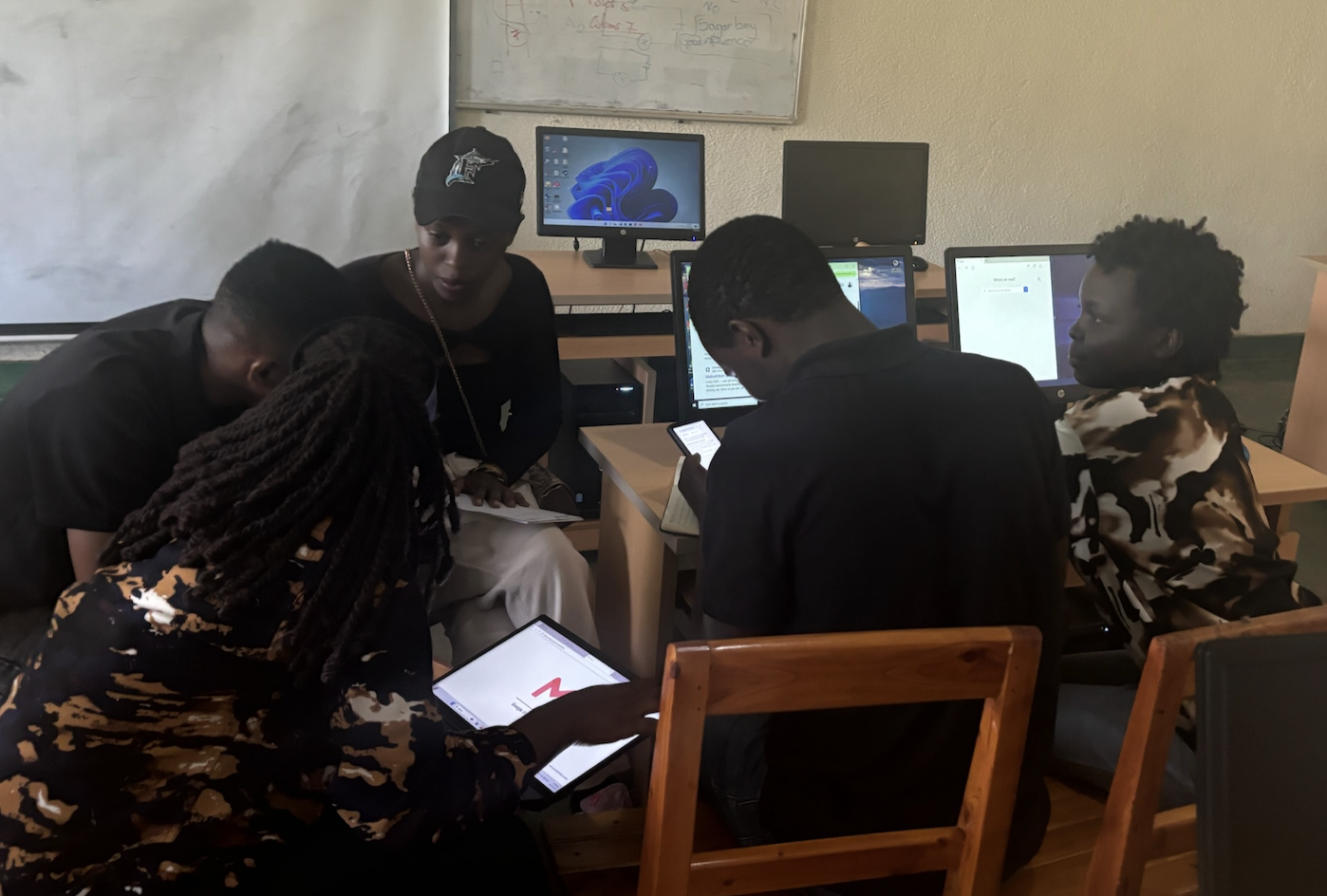 Students gathered around laptops and tablets in a computer lab